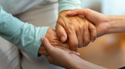 Asian woman doctor consoling senior patient with holding her hand. Private duty nurse visit and take care elderly woman on the bed at home. Home medical caregiving service and health insurance concept